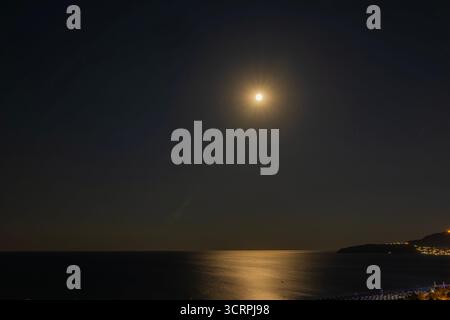 Heller Vollmond, der nachts über dem Mittelmeer leuchtet, mit goldener Reflexion auf dem Wasser und beleuchteter Küste. Griechenland. Stockfoto