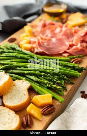 Verwöhnen Sie sich mit einer wunderschön gestalteten Wurstplatte mit lebhaftem Spargel, herzhaftem Wurstwaren, verschiedenen Käsesorten und frisch geröstetem Brot, ideal für Stockfoto