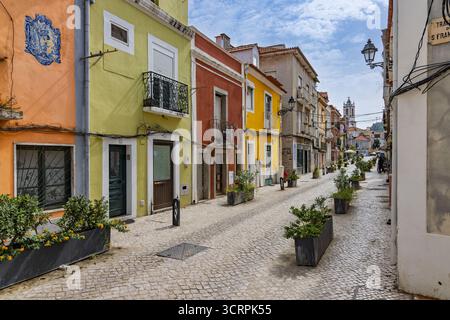 Eine kopfsteingepflasterte Straße im historischen Zentrum von Setubal ist gesäumt von charmanten, traditionellen Gebäuden mit farbenfrohen Fassaden in Gelb, Orange, Stockfoto