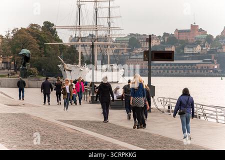 Stockholm, Schweden - 22. September 2014 - Menschen, die entlang der Uferpromenade mit Segelboot im Hintergrund laufen. Stockfoto