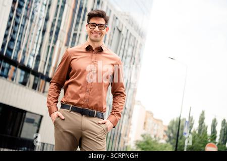 Selbstbewusster junger Geschäftsmann in formeller Kleidung posiert auf einer Stadtstraße mit modernen Bürogebäuden im Hintergrund Stockfoto