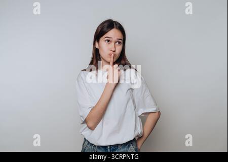 Junge Frau in lässiger Kleidung, die mit dem Finger auf den Lippen nachdenkt. Stockfoto