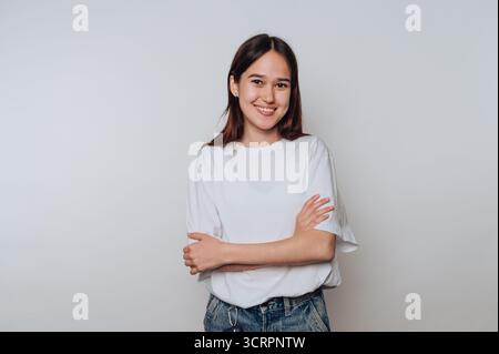 Eine junge Frau lächelt mit überkreuzten Armen vor einem schlichten Hintergrund. Stockfoto