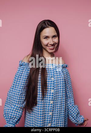 Lächelnde Frau in blauem kariertem Kleid vor rosa Hintergrund. Stockfoto
