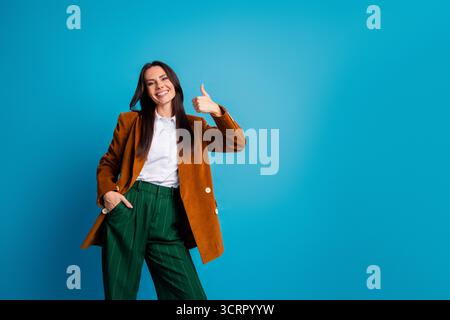 Selbstbewusste junge Geschäftsfrau in stilvoller Formalwear posiert mit fröhlichem Auftreten vor einem leuchtend blauen Hintergrund Stockfoto