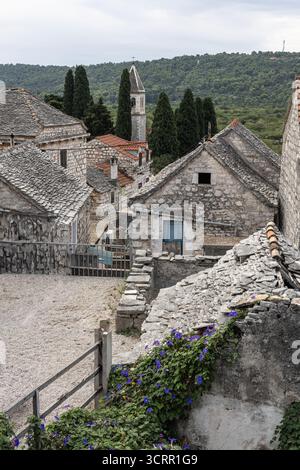 Ein rustikales Steindorf mit Kirchturm, Schiefer- und Ziegeldächern, engen Gassen und üppigen grünen Hügeln in der Ferne. Ruhig, historisch Stockfoto