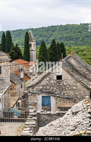 Ein rustikales Steindorf mit Kirchturm, Schiefer- und Ziegeldächern, engen Gassen und üppigen grünen Hügeln in der Ferne. Ruhig, historisch Stockfoto