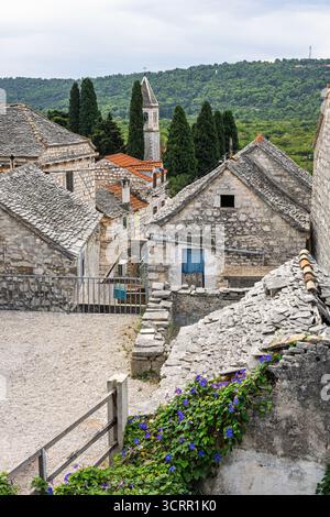 Ein rustikales Steindorf mit Kirchturm, Schiefer- und Ziegeldächern, engen Gassen und üppigen grünen Hügeln in der Ferne. Ruhig, historisch Stockfoto