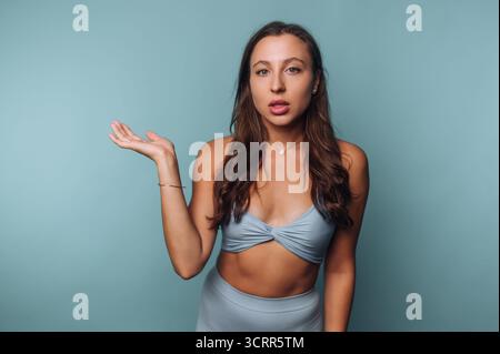 Ein junges Model steht vor blauem Hintergrund und trägt ein trendiges Outfit. Sie zeigt einen selbstbewussten Ausdruck, während sie mit der Hand Gesten macht und Inte hinzufügt Stockfoto