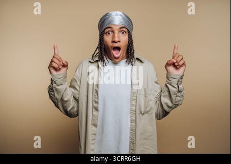 Ein junger Mann mit silbernem Kopftuch hebt beide Hände in die Luft und sieht begeistert und überrascht aus. Stockfoto