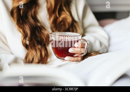 Eine Frau hält eine Tasse Tee in der Hand. Entspannende Morgenmomente zu Hause. Gemütliche Atmosphäre mit warmem Kräutergetränk. Freizeit- und Komfortkonzept. Stockfoto