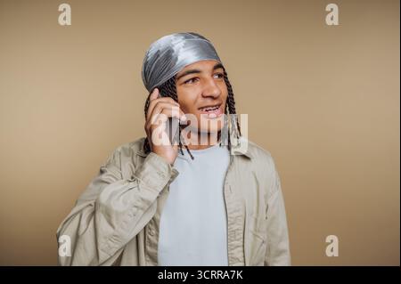 Junger Mann mit Zöpfen, der einen durag trägt und mit einem Smartphone spricht. Stockfoto