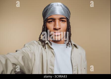 Junger Mann mit geflochtenen Haaren, der ein silbernes durag und beiges Hemd trägt. Stockfoto