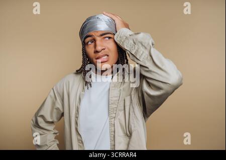 Junger Mann mit verwirrtem Ausdruck, der eine durag und lässige Kleidung trägt. Stockfoto
