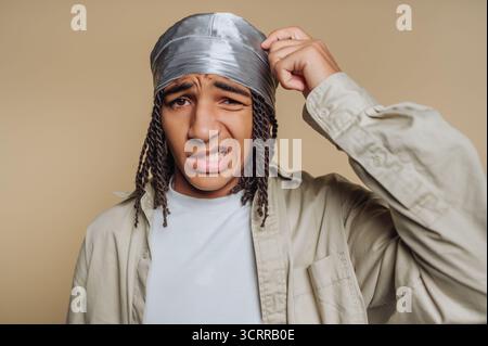 Ein junger Mann mit verwirrtem Ausdruck, der einen durag und lässige Kleidung trägt. Stockfoto