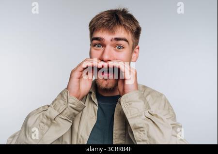 Junger Mann mit überraschtem Ausdruck, Hände umrahmen den Mund. Stockfoto