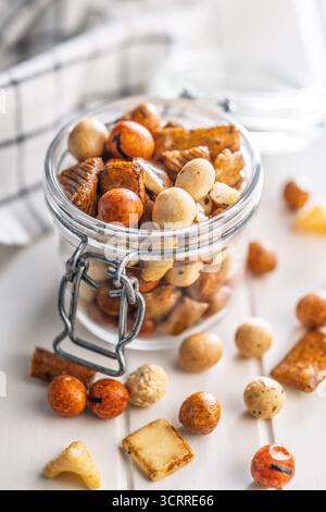 Gesalzener Snack. Beschichtete Erdnüsse und Mini-Cracker im Glas auf einem weißen Tisch. Stockfoto