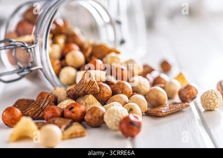 Gesalzener Snack. Beschichtete Erdnüsse und Mini-Cracker im Glas auf einem weißen Tisch. Stockfoto