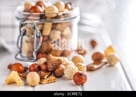 Gesalzener Snack. Beschichtete Erdnüsse und Mini-Cracker im Glas auf einem weißen Tisch. Stockfoto