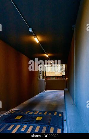 Kontrastierender schmaler Eingang zu einem Parkplatz oder einer Garage mit niedriger schwarzer Decke und gelben Lampen Stockfoto