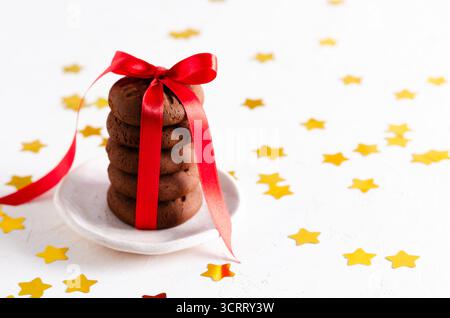 Gestapelte Schokoladenkekse mit einem roten Band und goldenen Sternen auf weißem Hintergrund. Horizontales Format und Kopierraum. Stockfoto