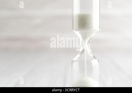 Nahaufnahme von weißem Sand, der durch die Zwiebeln einer Sanduhr läuft und die Verlaufzeit in einem Countdown bis zu einem Termin auf weißem Hintergrund misst. Stockfoto