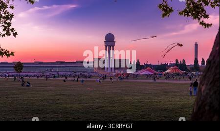 Während des riesigen Drachenfestes schweben Drachen über Berlins ehemaligen Flughafen Tempelhof bei Sonnenuntergang – lebendiger Himmel und Silhouetten. Stockfoto