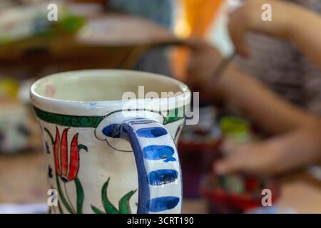 Dieses Bild zeigt einen wunderschön handgefertigten Keramikbecher mit lebhaften Tulpenmotiven, die eine warme und einladende Atmosphäre zum Genießen eines Stockfoto