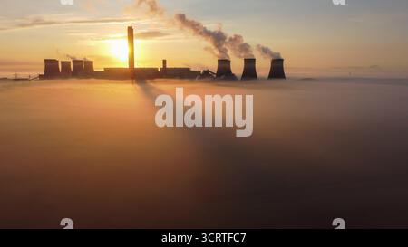Drohnenansicht des Kraftwerks Drax bei Sonnenaufgang, mit Kühltürmen und Schornsteinen, die Dampf aussenden, mit langen Schatten auf nebligen, tief liegenden Nebel Stockfoto