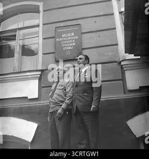 Ein formelles schwarz-weißes Archivporträt aus den 1960er Jahren, das einen dekorierten sowjetischen Kriegsveteranen und einen Beamten der Kommunistischen Partei zeigt, der gemeinsam in Swiatohirsk, der ukrainischen SSR, posiert. Sie stehen stolz unter dem Zeichen des örtlichen Museums für Revolutionäre, Militär- und Arbeiterherrschaft. Dieses Foto ist eine klassische symbolische Darstellung der Säulen der sowjetischen Gesellschaft: Der heldenhafte Veteran, der die vergangenen Opfer der Nation verkörpert, und der Beamte, der die gegenwärtige Macht des Staates repräsentiert, vereint unter dem Banner der institutionalisierten Geschichte Stockfoto