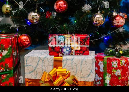Wunderschön gewickelte Weihnachtsgeschenke mit Schleifen und Bändern unter einem verzierten Baum mit glänzenden Kugeln und festlichen Ornamenten. Stockfoto