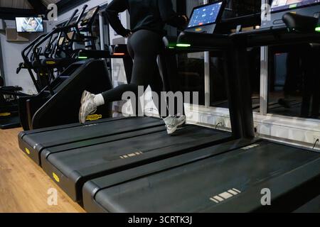 Eine Person, die auf einem Laufband in einem Fitnessstudio läuft. Die Person trägt schwarze Hosen und weiße Schuhe Stockfoto