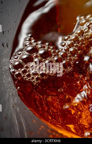 Goldenes Getränk wird in das Glas gegossen und erzeugt wunderschöne Wellen und Spritzer. Selektiver Fokus. Makroaufnahme. Stockfoto