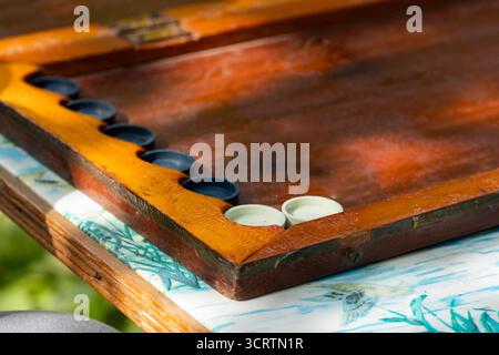Nahaufnahme einer Person, die draußen Backgammon spielt. Traditionelles Holzbrett mit Würfeln und Spielstücken, Symbol für Freizeit, Strategie und kulturellen Pastim Stockfoto