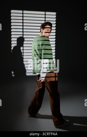 Der junge Mann steht selbstbewusst in einem trendigen Outfit und schafft ein künstlerisches Schattenspiel. Stockfoto