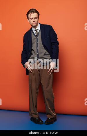 Trendiger Teenager steht selbstbewusst in modischer Kleidung vor einer orangefarbenen Wand. Stockfoto