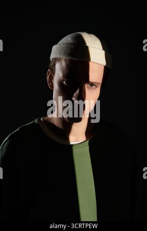 Ein junger Mann steht selbstbewusst im Schatten und drückt seinen einzigartigen Stil und seine junge Energie aus. Stockfoto