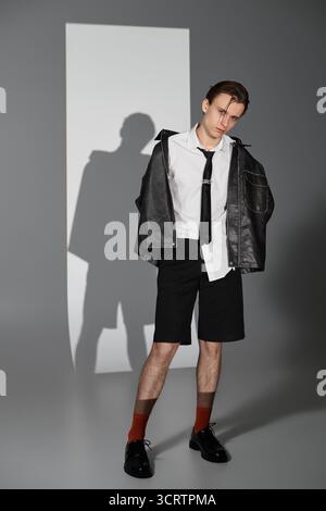Junger Mann in trendigem Outfit steht selbstbewusst in einer minimalistischen Umgebung. Stockfoto