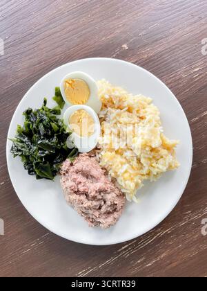 Nahrhafte Mahlzeit mit geriebenem Thunfisch, gekochtem Ei, Reis mit Linsen und frischem Wakam-Algensalat wird auf Teller serviert. Geschirr steht auf rustikalem Holz Stockfoto