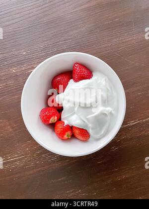 Frische Erdbeeren werden mit cremigem griechischem Joghurt auf Teller serviert. Dessert steht auf rustikalem Holztisch, bereit zum Genießen Stockfoto