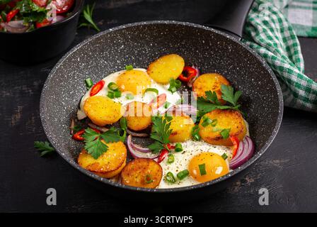 Spiegeleier und Kartoffeln mit Zwiebeln und Chili auf dunklem Hintergrund. Stockfoto