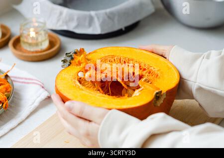 Nahaufnahme einer Frau mit halbem Kürbis mit Händen auf hölzernem Schneidebrett Stockfoto