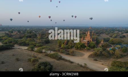Aus der Vogelperspektive schweben Heißluftballons ruhig über antike Tempel und üppige Landschaften, die in das weiche, warme Licht der Dämmerung getaucht sind, Old Bagan, Mandalay Re Stockfoto