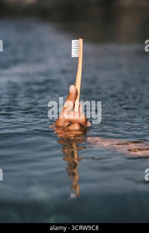 Nahaufnahme der Hand, die Bambuszahnbürste über der Wasseroberfläche hält Stockfoto