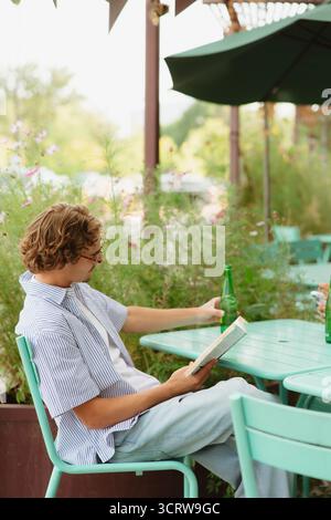 Ein Mann, der sich draußen entspannt und ein Buch mit einer Flasche Wasser liest Stockfoto