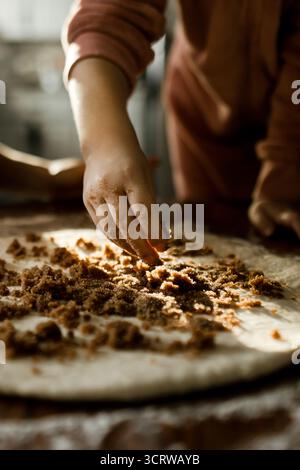 Kind streut braunen Zucker auf Teig in der Küche Stockfoto