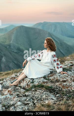 Frau in traditioneller Kleidung sitzt barfuß auf einem Berggipfel. Stockfoto