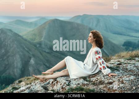 Frau in traditioneller Kleidung sitzt barfuß auf einem Berggipfel. Stockfoto