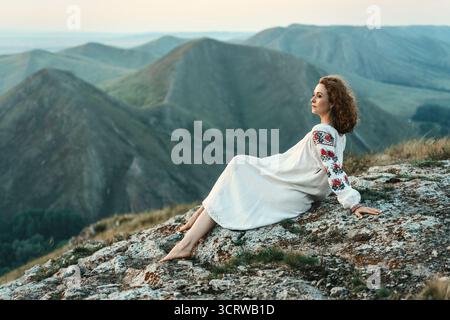 Frau in traditioneller Kleidung sitzt barfuß auf einem Berggipfel. Stockfoto