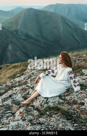 Frau in traditioneller Kleidung sitzt barfuß auf einem Berggipfel. Stockfoto
